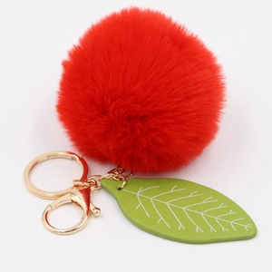 Detailed view of red faux fur pompom keychain with green leaf charm and gold hardware