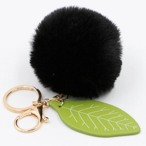 Close-up of fluffy black faux fur pom pom keychain with green leather leaf and gold clasp
