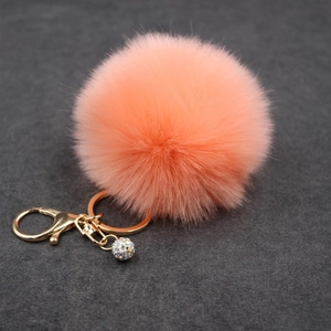 Detail of coral pink faux fur pompom keychain with golden clasp and sparkling crystal ball