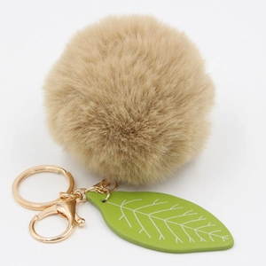 Detail of the soft khaki faux fur ball keychain with green leaf charm and gold hardware