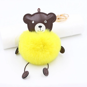 Detail of cute brown leather bear keychain with yellow plush pom-pom and metallic ring