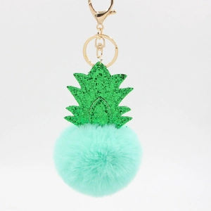 Close-up of mint green fur pompom pineapple keychain with green glitter leaves and gold clasp