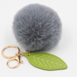 Detail of grey faux fur pom pom keychain with green leaf charm and gold metal clasp