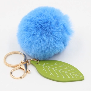 Detailed view of plush blue fur ball keychain with green leaf charm and gold hardware
