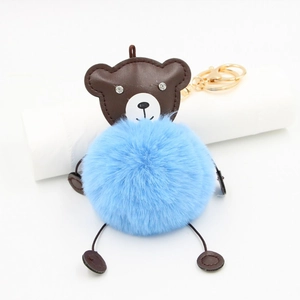 Detail of a brown bear leather keychain with a large sky blue faux fur pompom and gold clasp