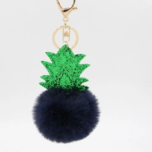 Close-up of fluffy dark blue plush ball and sparkly green pineapple leaf pendant