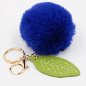 Detailed view of fluffy navy faux rabbit fur pom pom with green leaf charm on golden keychain