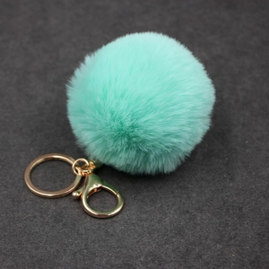 Détail d'un porte-clés pompon en fausse fourrure vert menthe avec fermoir mousqueton doré