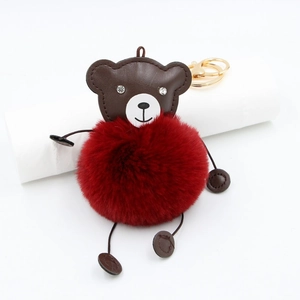 Detail of red faux fur pompom bear keychain with gold metal ring on white surface