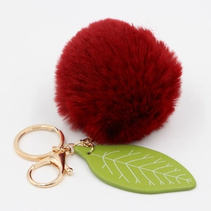 Macro detail of red faux fur pompom keychain with green leaf and golden metal hardware