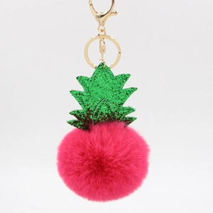 Detail view of a pink pineapple pom-pom keychain with green glitter leaves and gold clasp