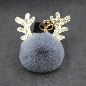 Close-up of a grey plush pompom keychain with golden sequin antlers and a metallic clip