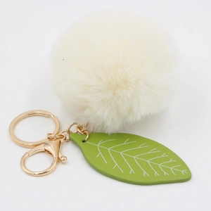 Detail of soft cream faux fur ball and green leaf charm with golden lobster clasp