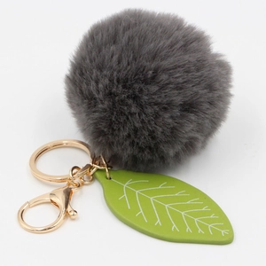 Close-up of faux rabbit fur pom pom with green leaf charm and gold lobster clasp