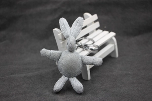 Gros plan d'un porte-clés peluche lapin gris argenté brillant sur un banc blanc en bois