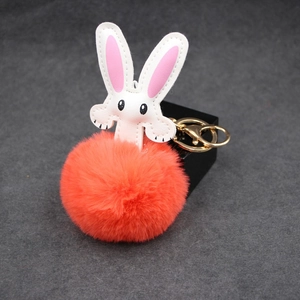 Close-up of fluffy orange pompom keychain with white leather rabbit head and gold metal clasp