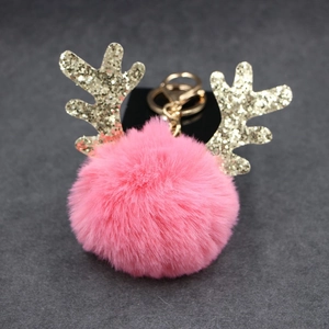 Detail of pink faux fur pompom keychain with golden glitter reindeer antlers and lobster clasp