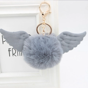 Close-up of grey faux fur pompom keychain with angel wings and golden metal clasp