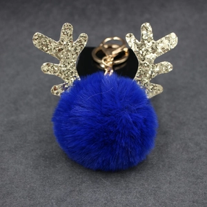 Detailed view of navy blue faux fur pompom keychain with golden sequin reindeer antlers