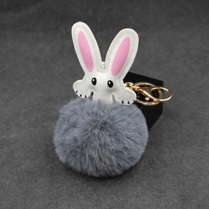 Close-up of white rabbit charm with fluffy grey pompom and gold metal keychain hook