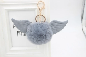 Close-up of a grey faux fur pompom keychain with angel wings and golden metal clasp