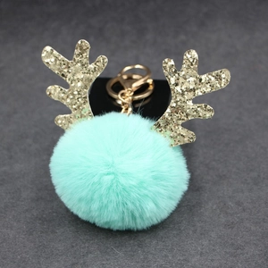 Detail of mint green plush ball keychain with golden glitter reindeer antlers on black card