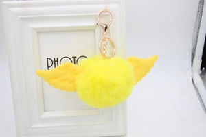 Detail of bright yellow faux fur pompom keychain with cute angel wings and gold clasp