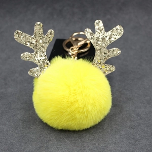 Detail of yellow plush pompom keychain with golden reindeer antlers and metal clip