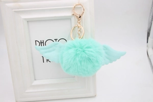Detail of mint green faux fur pompom keychain with angel wings and gold lobster clasp