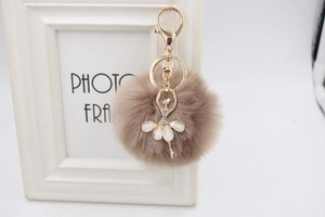Detailed view of plush beige pompom keychain with a rhinestone gold ballerina charm