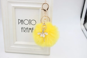 Detailed close-up of yellow faux fur pompom keychain with rhinestone angel ballerina charm