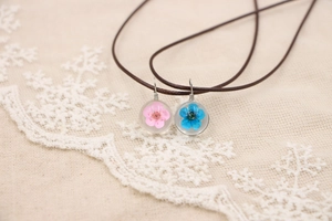 Détail de pendentifs en verre faits main avec de vraies fleurs séchées sur dentelle