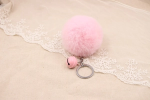 Detailed view of pink faux rabbit fur pom pom keychain with a bell on white lace