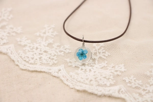Gros plan d'un pendentif en forme de fleur bleue séchée dans une boule de cristal