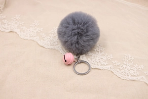 Close-up of grey faux fur pom pom keychain with pink metal bell on linen fabric