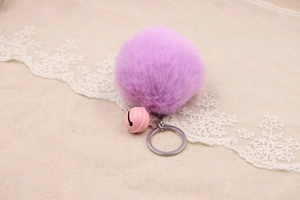 Close-up of a soft purple faux fur pompom keychain with a pink bell on canvas background