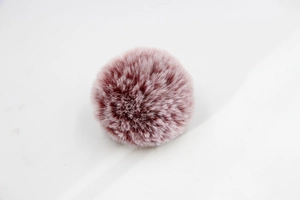 Detail view of a fluffy dusty pink faux rabbit fur pom pom for bags and keychains
