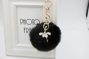 Detail of black faux fur ball keychain featuring a gold ballet dancer with rhinestones