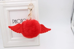 Detail view of red faux fur pompom keychain with angel wings and gold lobster clasp