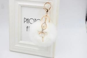 Detail of white pom-pom keychain with rhinestone ballerina pendant and gold lobster clasp