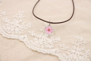 Gros plan d'un pendentif sphère avec une vraie fleur rose sur cordon en cuir brun
