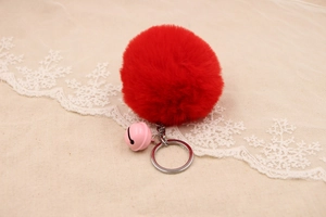 Detail of red faux fur pompom keychain with a pink bell and silver metal ring