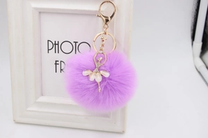 Detail of purple fluffy keychain featuring a gold ballet dancer with rhinestones and fur