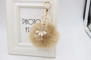 Detailed close-up of a khaki faux fur ball with a gold ballerina pendant on frame