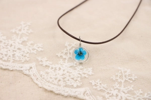 Gros plan du pendentif rond en résine avec fleur séchée bleue sur dentelle blanche