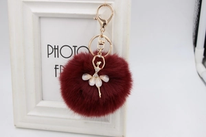 Detail of burgundy faux fur pompom keychain with gold ballerina charm and pearl accents