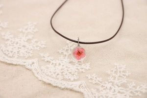 Détail macro du pendentif en verre fait main avec une vraie fleur séchée rose et un cordon