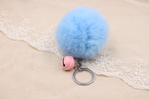 Close-up of soft sky blue faux fur pompom keychain with a pink bell and metal ring