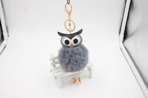 Détail du porte-clés pompon hibou gris posé sur un petit banc blanc décoratif