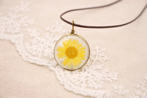 Gros plan détaillé d'un pendentif en verre avec une vraie fleur de marguerite jaune sur lin